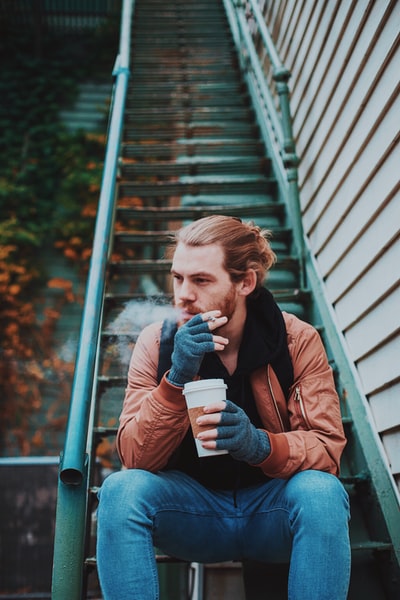 男子坐在楼梯上吸烟的选择性聚焦摄影